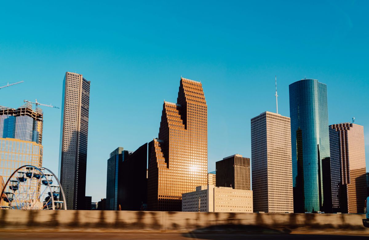 Downtown skyline of modern glass and concrete skyscrapers lit by warm sunlight with a Ferris wheel at left.