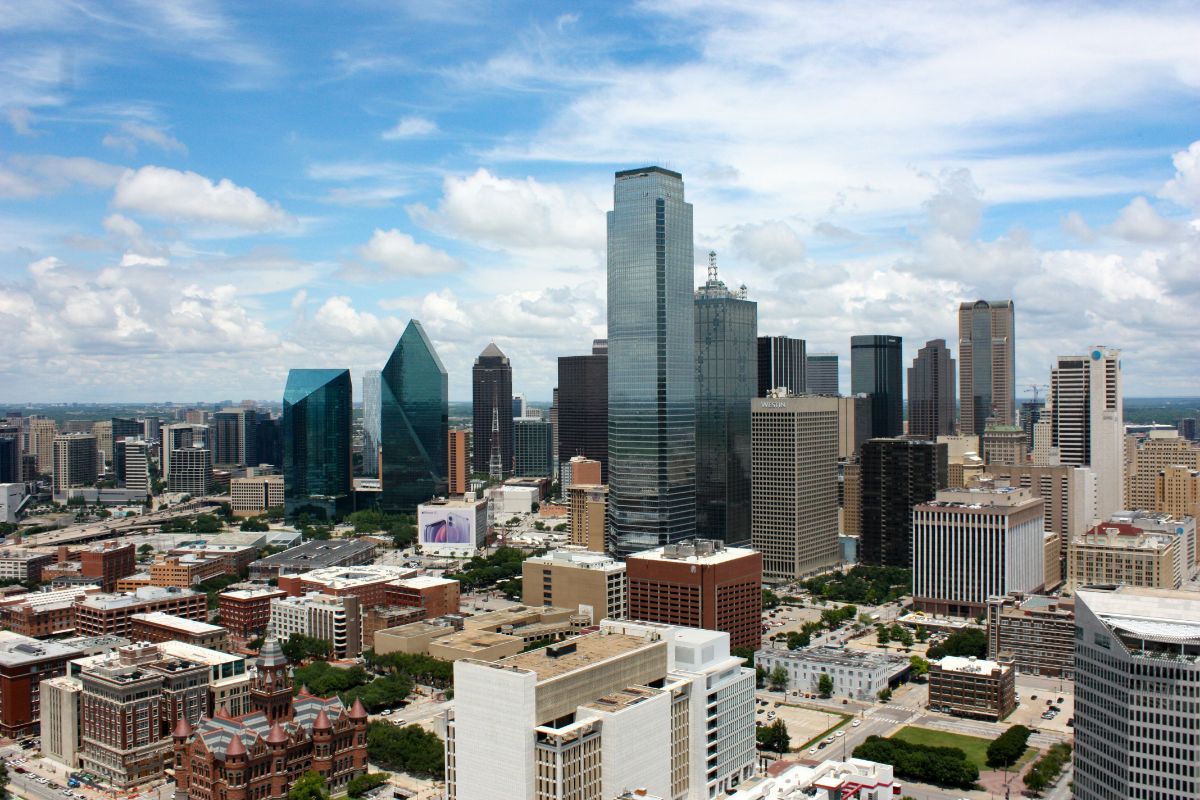 Aerial view of a downtown skyline with reflective glass skyscrapers and a distinctive triangular tower under a blue sky.